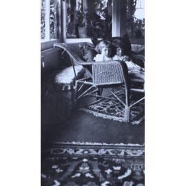 Two small girls sitting on a cane lounge in a sunroom