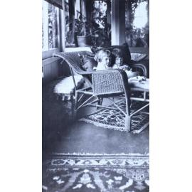 Two small girls sitting on a cane lounge in a sunroom