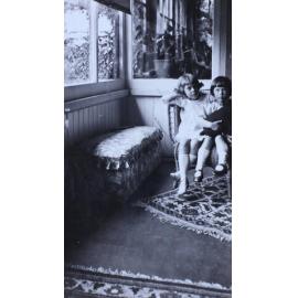 Two young girls sitting in a cane chair in a sunroom