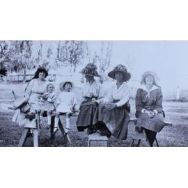 Group of women and children sitting on a plank in the garden