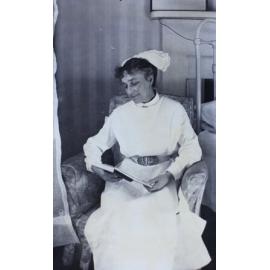 Nurse sitting in a chair beside a bed reading