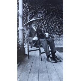 Man sitting on the verandah wearing an Asian style hat