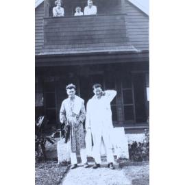 Two unidentified men in pyjamas standing in front of a house