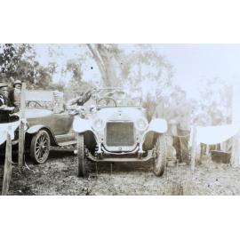 Group of unidentified men standing around a man seated in a car