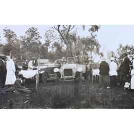 An unidentified man stand in a car speaking to a group of man and women