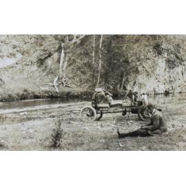 Unidentified man sitting on the grass beside a creek