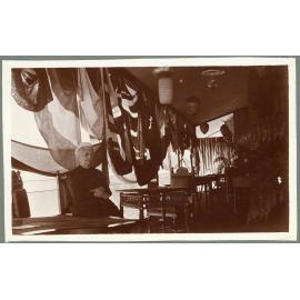 Woman seated on verandah with flags at Booloominbah