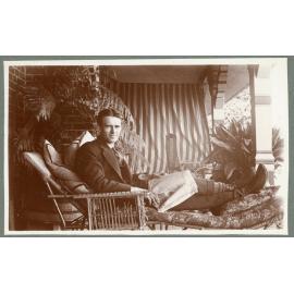 Man lounging with a newspaper at Booloominbah, c.1919