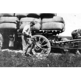 Driver removing mud from wheel of bogged horse wagon with load of wool bales