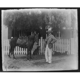Man with horse and three dogs in front of a picket fence, 1904