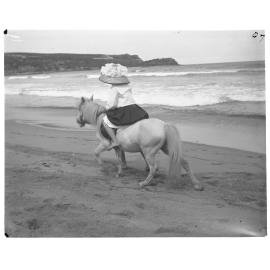 Girl riding a pony along a seashore, 1907