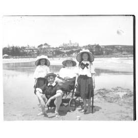 A woman in a wheelchair with two girls and a boy on a beach, 1907