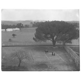Elevated view of a tennis court with two women and a child on horseback