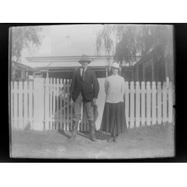 Man and woman standing outside house with picket fence