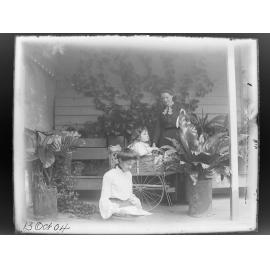 Two women and a child on a verandah with potted plants, 1904