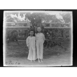 Two children in pyjamas standing in front of a grape vine, 1904