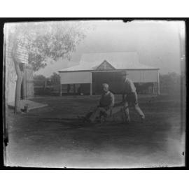 Man pushing another man in a wheelbarrow