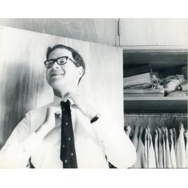 John Ryan adjusting his tie in front of a closet