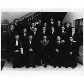 Group of men in academic dress beneath a staircase