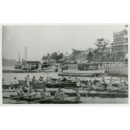 View of row boats and steamers on a river with the town in the background [Lismore]