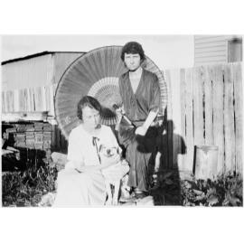 Clare Chamberlain (seated with dog) and Vere Chamberlain in front of a parasol and paling fence