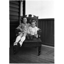 Two unidentified children sitting on a chair on the verandah of 63 Barney Street, Armidale