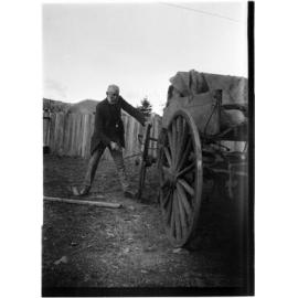 Unidentified older man standing by a wooden cart