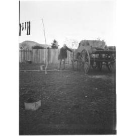 Unidentified older man standing by a wooden cart