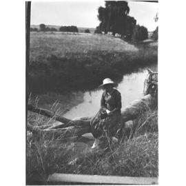 Unidentified woman sitting on a log by a creek